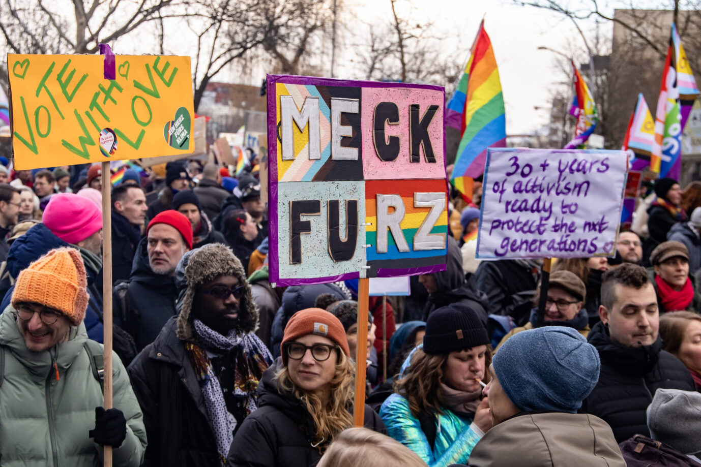 Bunt gekleidete Leute sind auf einem Christopher Street Day (CSD) unterwegs und halten ein Anti-CDU-Plakat hoch, das Friedrich Merz (CDU) beschimpft, Februar 2025