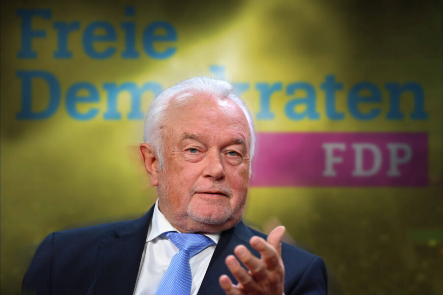 Wolfgang Kubicki vor einem verschwommenen FDP-Hintergrund mit dem Schriftzug „Freie Demokraten“ und dem Logo der Partei, spricht gestikulierend in die Kamera.