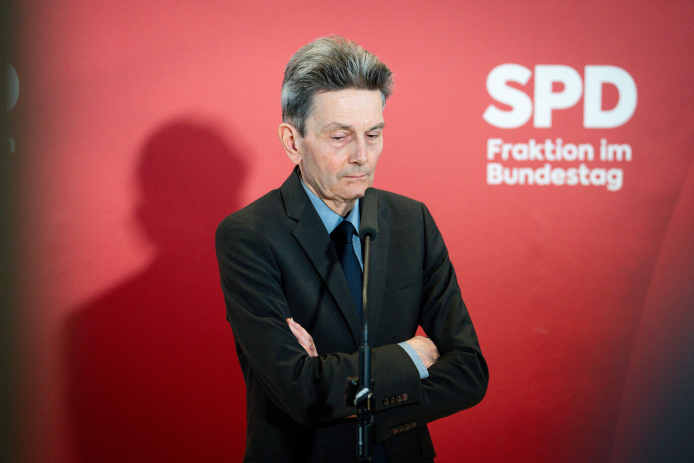 Rolf Mützenich, langjähriger Vorsitzender der SPD-Bundestagsfraktion, steht mit verschränkten Armen vor einem Mikrofon. Er blickt ernst zu Boden, im Hintergrund das rote Logo der SPD-Fraktion im Bundestag. Die Szene vermittelt Nachdenklichkeit und politische Anspannung. Das Bild entstand bei einer Pressekonferenz im Bundestag. Rolf Mützenich ringt mit seiner Rolle in der SPD: Der Streit um den Rußland-Kurs hat ihn „irritiert“. Foto: Foto: IMAGO / Political-Moments