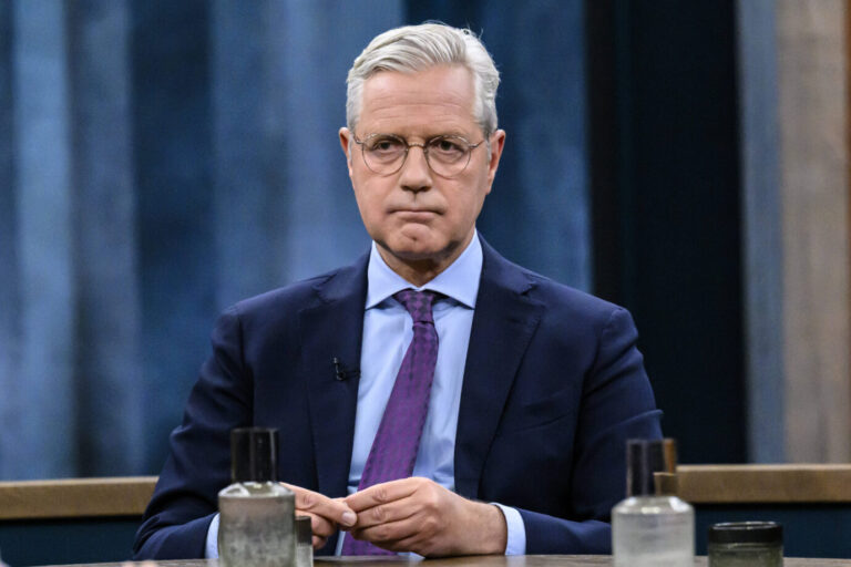 Norbert Röttgen, CDU-Außenpolitiker, mit ernster Miene in einem Fernsehstudio. Er trägt einen dunkelblauen Anzug, ein hellblaues Hemd und eine lilafarbene Krawatte. Im Vordergrund stehen mehrere Wassergläser und Flaschen auf einem Studiotisch. Die Bildszene wirkt konzentriert und sachlich. Das Bild eignet sich zur Bebilderung politischer Interviews oder außenpolitischer Debatten.