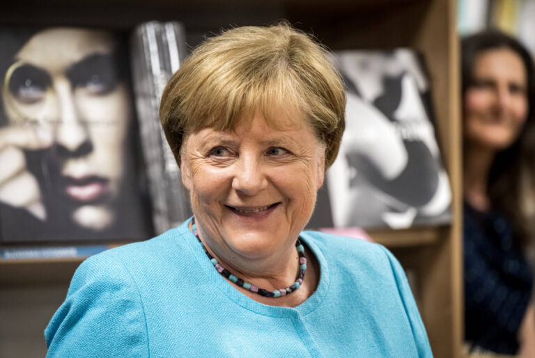 Die ehemalige Bundeskanzlerin Angela Merkel (CDU) steht in einem türkisen Pullover irgendwo in der Gegend rum und grinst diabolisch – den aktuellen Asyl-Kurs ihrer Partei mag sie gar nicht, weil zu wenig Migranten ins Land kommen