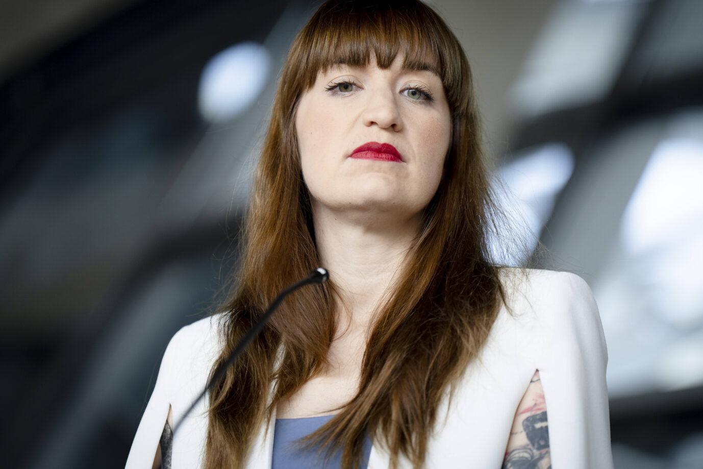 Heidi Reichinnek, Fraktionsvorsitzende der Linkspartei im Bundestag, blickt mit ernstem Gesichtsausdruck in die Kamera. Im Vordergrund ist ein Mikrofon zu sehen, im Hintergrund die verschwommene Glasarchitektur des Bundestags. Sie trägt einen weißen Blazer und hat sichtbare Tätowierungen an den Armen. Mit Drohgebärden gescheitert: Heidi Reichinnek verfehlt die Mehrheit fürs Kontrollgremium. Foto: IMAGO / Bernd Elmenthaler