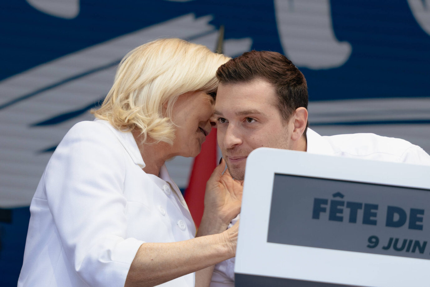 Links sieht man die RN-Chefin Marine Le Pen, die dem rechts sitzenden Jordan Bardella etwas ins Ohr flüstert