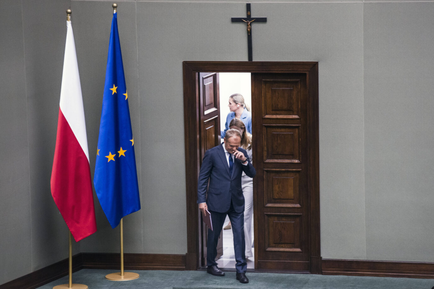 Der polnische Ministerpräsident Donald Tusk betritt am 11. Juni 2025 den Plenarsaal des Sejm in Warschau zur Vertrauensabstimmung über sein Kabinett. Im Hintergrund zwei Mitarbeiterinnen, links die Flaggen Polens und der Europäischen Union, darüber ein Kreuz. Die Szene symbolisiert die politische Spannung nach der knappen Niederlage des von Tusk unterstützten Präsidentschaftskandidaten Rafał Trzaskowski bei der Stichwahl gegen den rechtskonservativen Karol Nawrocki. Polens Premierminister Donald Tusk im Sejm: Sein Lager zweifelt die Präsidentschaftswahl an. Foto: IMAGO / SOPA Images