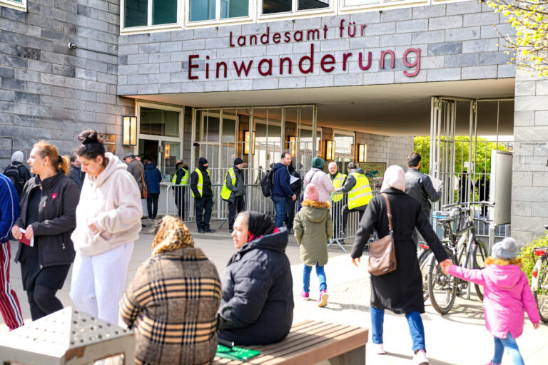 Ort der Einbürgerung: Menschen warten vor dem Landesamt für Einwanderung in Berlin. Sicherheitskräfte mit Warnwesten stehen vor dem Eingang, Besucherinnen mit Kopftuch und Kinderkleidung bewegen sich zum Gebäude. Im Vordergrund sitzen und stehen Personen in Winterkleidung. Schlange vor dem Landesamt für Einwanderung in Berlin: Beamte sollen gegen Bezahlung eingebürgert haben. Foto: picture alliance / SULUPRESS.DE | Vladimir Menck/SULUPRESS.DE