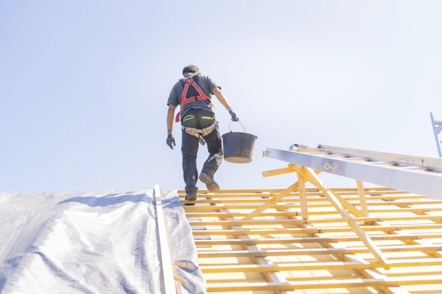 Ein Arbeiter in Sicherheitskleidung klettert eine Leiter hoch, um auf einem Dach zu arbeiten, bei sonnigem Wetter, Dachsanierung, Hausbau, Pforzheim, Deutschland, Europa. Gebäudetyp E löst die Probleme nicht.