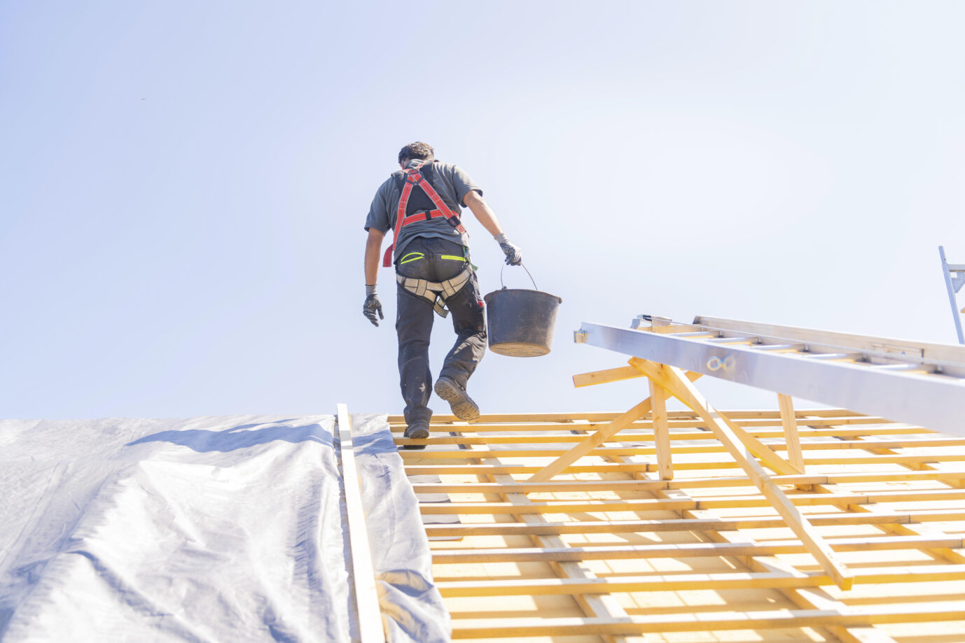 Ein Arbeiter in Sicherheitskleidung klettert eine Leiter hoch, um auf einem Dach zu arbeiten, bei sonnigem Wetter, Dachsanierung, Hausbau, Pforzheim, Deutschland, Europa. Gebäudetyp E löst die Probleme nicht.