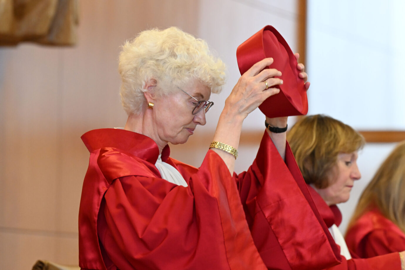 Doris König, Vizepräsidentin des Bundesverfassungsgerichts, und Christine Langenfeld, Richterin im Zweiten Senat, beim feierlichen Aufsetzen ihrer roten Baretts während der Urteilsverkündung. Das Verfahren betrifft die Verfassungsbeschwerde zweier Jemeniten gegen die Mitwirkung Deutschlands an US-Drohneneinsätzen über die Air Base Ramstein. Beide tragen die rote Amtstracht des Gerichts. Im Hintergrund ist eine weitere Richterin zu sehen, leicht unscharf.