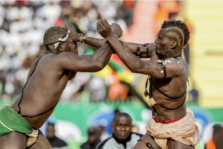 Zwei schwarze Männer stehen sich gegenüber und kämpfen – es handelt sich um zwei Teilnehmer eines traditionellen Wrestling-Turniers in Gambia.