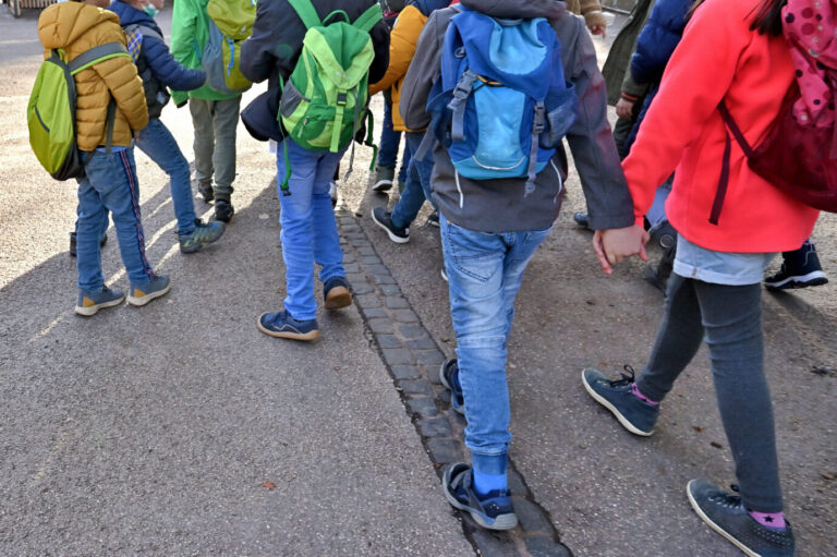 Mehrere Kinder mit Schulranzen laufen über eine Straße – ein Symbolbild für einen Schulausflug, so wie sie eine sechste Klasse einer Berliner Schule nach Brandenburg unternahm – und dabei wohl nicht rassistisch attackiert wurde, wie zuvor behauptet