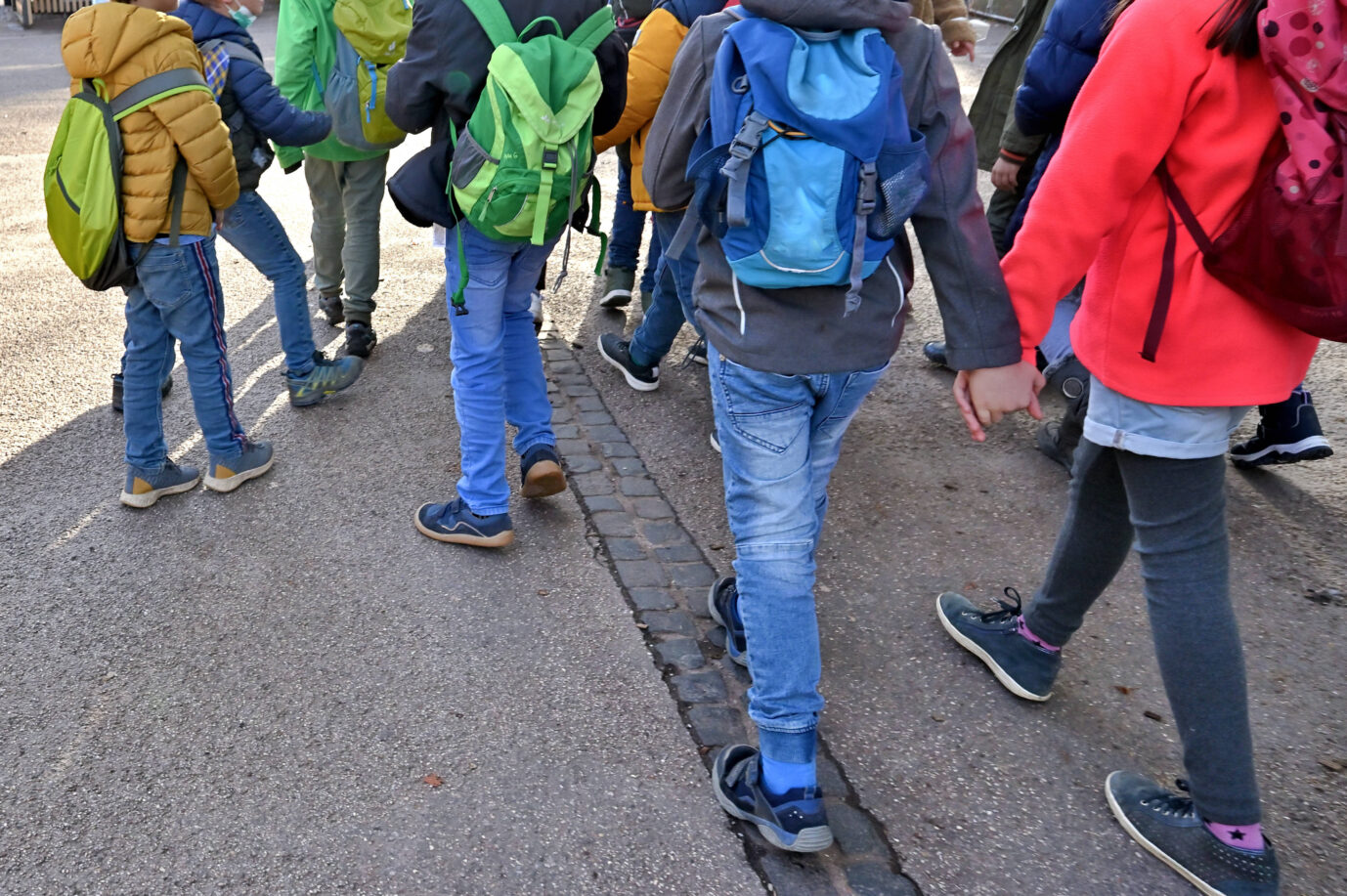 Mehrere Kinder mit Schulranzen laufen über eine Straße – ein Symbolbild für einen Schulausflug, so wie sie eine sechste Klasse einer Berliner Schule nach Brandenburg unternahm – und dabei wohl nicht rassistisch attackiert wurde, wie zuvor behauptet