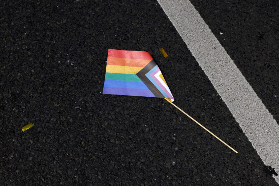 Die Flagge der Schwulen, Lesben und Transpersonen: Auf dem Asphalt einer Straße liegt eine kleine Progressive-Pride-Fahne mit abgebrochenem Holzstab. Die Szene stammt vom Christopher Street Day 2023 in Köln. Dort wurde unter dem Motto „Für Menschenrechte. Viele. Gemeinsam. Stark“ ein dreitägiges Straßenfest veranstaltet. Der ColognePride gilt nach Berlin als zweitgrößte CSD-Parade Deutschlands. Für die Parade am 9. Juli 2023 rechneten die Veranstalter mit etwa 1,5 Millionen Teilnehmern und Zuschauern entlang der Strecke. Das Foto symbolisiert den Kontrast zwischen bunter Sichtbarkeit und verletzlicher Realität sexueller Minderheiten im öffentlichen Raum. Eine Regenbogenfahne liegt auf dem Boden: Angreifer auf LSBTQ-Personen stammen meist nicht aus Deutschland. Foto: IMAGO / Panama Pictures