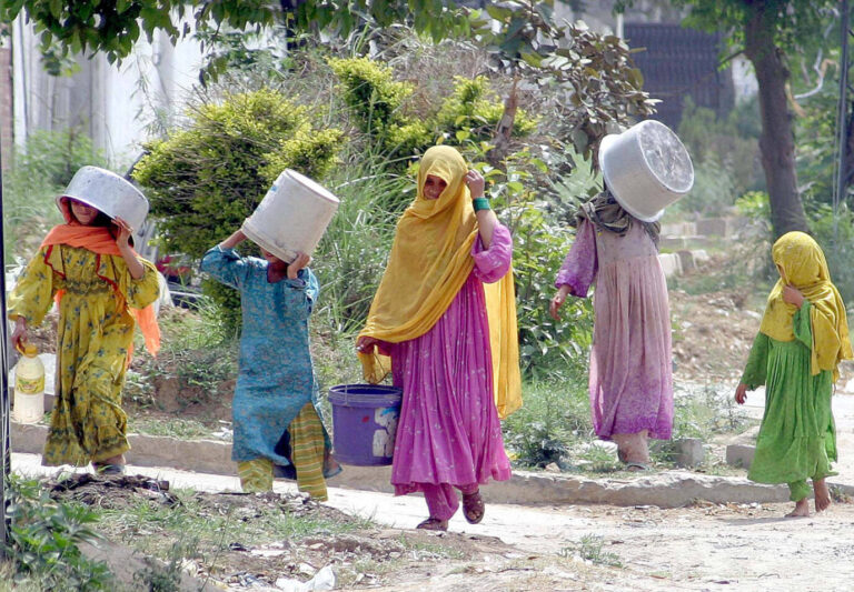 Mehrere verschleierte Frauen tragen leere Wasserbehälter – es handelt sich um Afghanen im pakistanischen Exil