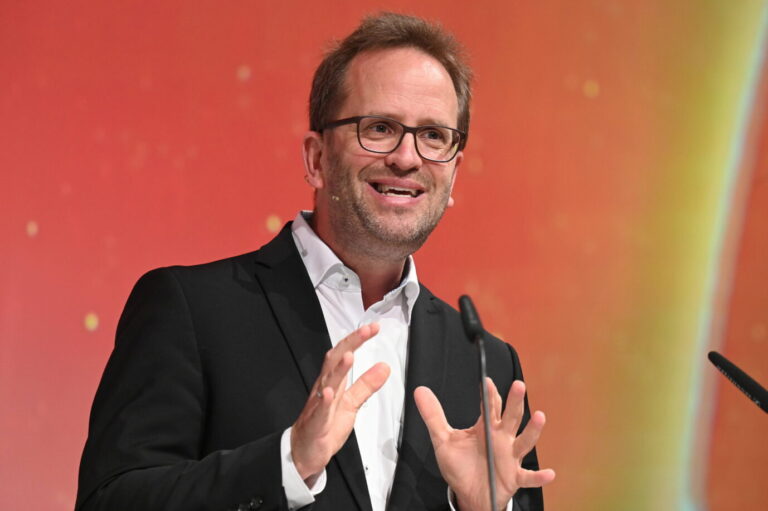 Vor einem roten Hintergrund steht der Chef der Bundesnetzagentur, Klaus Müller (Grüne) und lacht diabolisch, vermutlich freut er sich, daß Trusted Flagger wieder mal die Meinungsfreiheit beschneiden