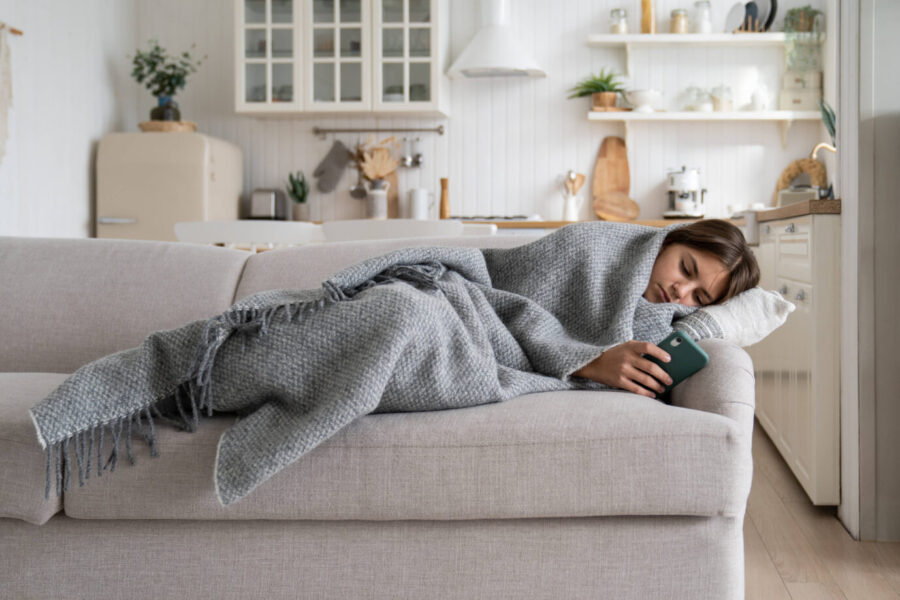 Auf einer Couch liegt eine junges Mädchen und hält ein Smartphone in der Hand – statistisch gesehen, wird sie dadurch schneller krank