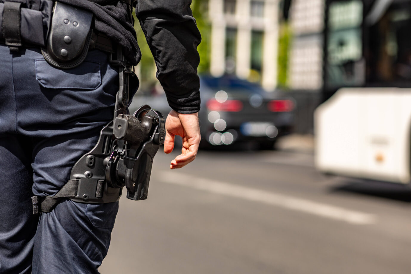 Ein Berliner Polizist steht im Vordergrund des Bildes, man sieht seine Pistole – in Berlin wurden heute nämlcih Wohnungen von Islamisten durchsucht