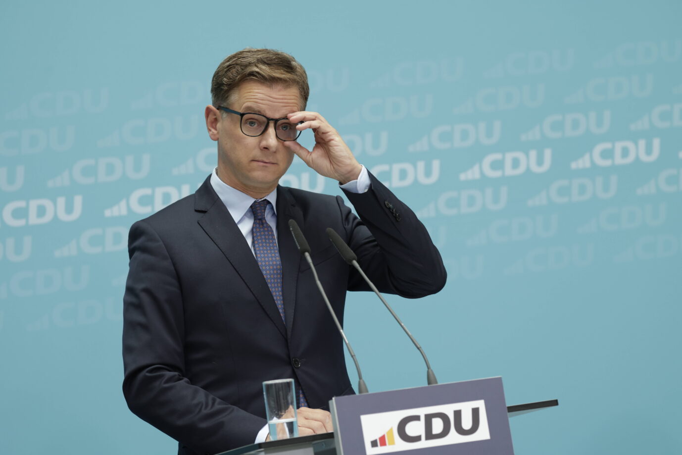 Die schwarz-rote Koalition will noch im Herbst das Bürgergeld reformieren, verspricht zumindest CDU-Generalsekretär Linnemann. Unterstützung bekommt die Union aus dem Handwerk. Ein Mann im Anzug und mit Brille steht vor einem Rednerpult mit CDU-Logo. Er blickt ernst und hebt die Hand zur Brille. Hinter ihm eine hellblaue Wand mit mehrfach wiederholtem CDU-Schriftzug. Zwei Mikrofone sind auf das Pult gerichtet. CDU-Generalsekretär Carsten Linnemann: „Dann muß das Geld komplett gestrichen werden.“ Foto: IMAGO / Metodi Popow