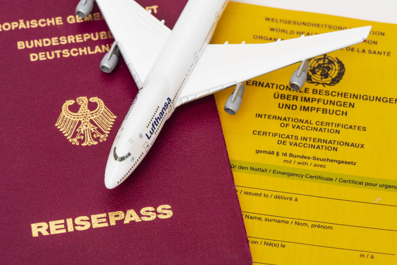 Das Bild zeigt ein Miniaturflugzeug, einen Reisepaß und einen Impfpaß. Es ist ein Symbolbild für Auswanderer.