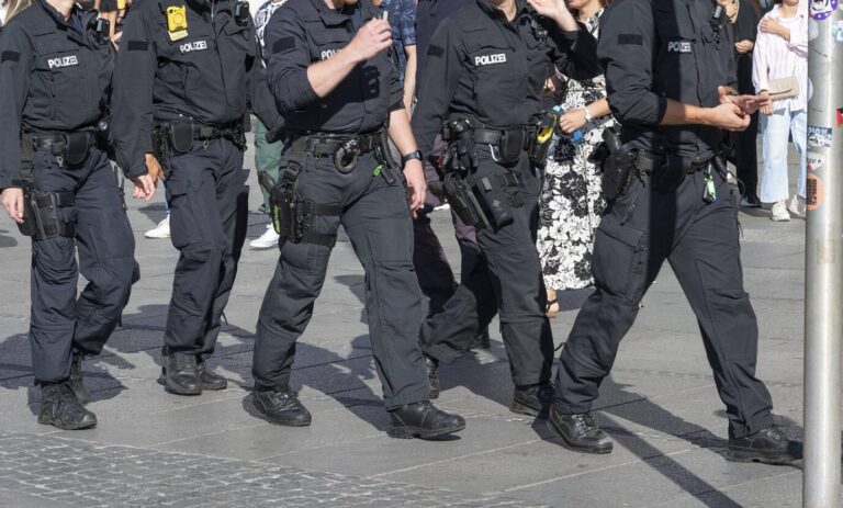Mehrere Polizisten in schwarzer Einsatzkleidung patrouillieren zu Fuß durch eine belebte Innenstadt. Sie tragen Ausrüstung wie Dienstwaffen, Bodycams und Funkgeräte. Im Hintergrund gehen Passanten, darunter Frauen in Sommerkleidung. Szene bei Tageslicht. Polizisten im Einsatz in der Innenstadt: Islamistische Netzwerke stehen im Fokus der Bundesanwaltschaft. Foto: IMAGO / imagebroker