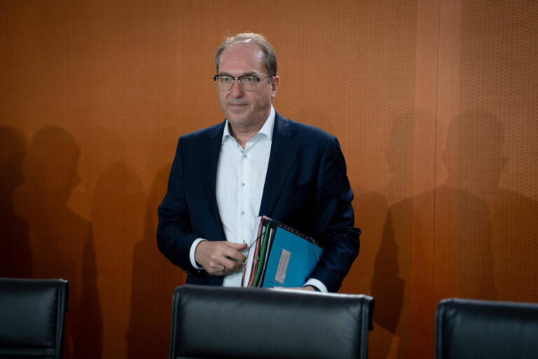 Ein Mann mittleren Alters mit Brille und Halbglatze steht in einem Konferenzraum vor einer holzvertäfelten Wand. Er trägt ein dunkles Sakko über einem weißen Hemd und hält mehrere Aktenordner unter dem Arm. Die Szene wirkt offiziell, möglicherweise Regierung oder Ministerium. Links und rechts fallen Schatten weiterer Personen auf die Wand. Zwei leere schwarze Ledersessel sind im Vordergrund sichtbar. Bundesinnenminister Alexander Dobrindt (CSU) bei einer Kabinettssitzung: Der Bayer stoppt das Berliner Aufnahmeprogramm. Foto: IMAGO / Bernd Elmenthaler
