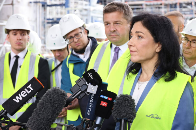 Wirtschaftsministerin Katharina Reiche spricht bei einem Werksbesuch des Gasekonzerns Linde vor Mikrofonen mehrerer Medienvertreter. Sie trägt eine gelbe Warnweste und einen blauen Blazer. Umgeben ist sie von Männern in Schutzhelmen und Sicherheitskleidung, im Hintergrund sind Industrieanlagen zu sehen. Bundeswirtschaftsministerin Katharina Reiche (CDU) besucht ein Chemiewerk: Das Bruttoinlandsprodukt fällt im zweiten Quartal. Foto: IMAGO / Frank Ossenbrink