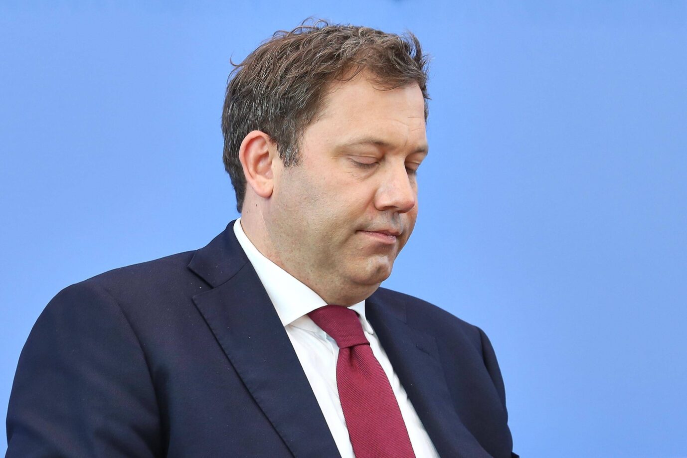 Ein Mann mittleren Alters im dunklen Anzug mit roter Krawatte und weißem Hemd steht vor einer blauen Wand. Er hat die Augen geschlossen und wirkt angespannt oder nachdenklich. Die Szene deutet auf einen offiziellen oder politischen Anlaß hin. Bundesfinanzminister Lars Klingbeil: Landkreise fordern vom Sozialdemokraten Kürzungen der Sozialleistungen. Foto: IMAGO / dts Nachrichtenagentur