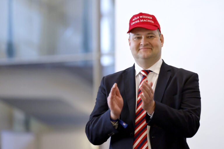 AfD-Politiker Christer Cremer trägt eine rote Kappe mit der Aufschrift Köln wieder groß machen und klatscht in die Hände. Er steht im Anzug mit gestreifter Krawatte in einem Innenraum und spricht im Wahlkampf über das Thema Mund verbieten. AfD-Kreissprecher Christer Cremer mit Wahlkampfmütze: Der Kölner AfD-Kreissprecher lehnt das Fairness-Abkommen ab. Foto: picture alliance / Panama Pictures | Christoph Hardt