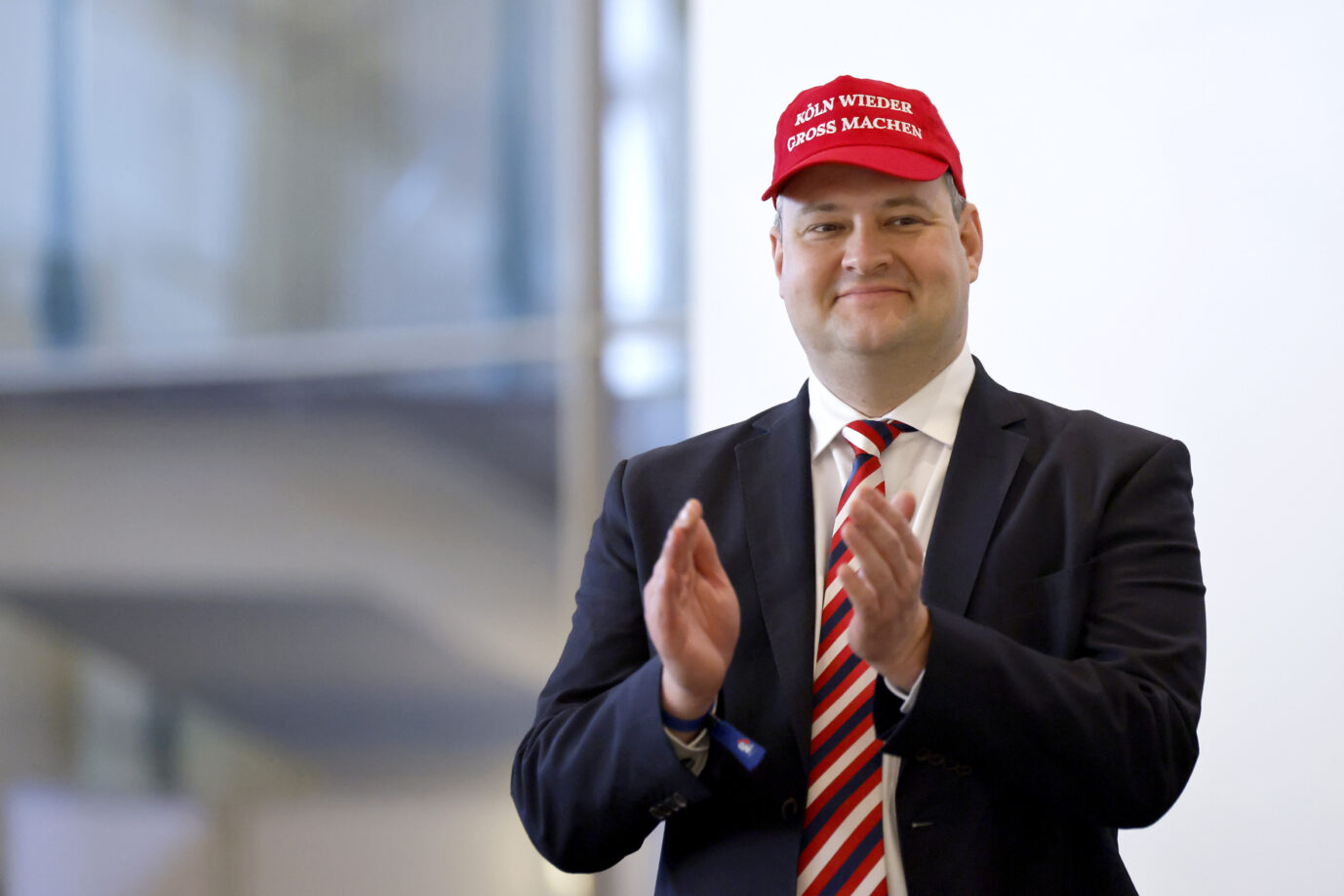 AfD-Politiker Christer Cremer trägt eine rote Kappe mit der Aufschrift Köln wieder groß machen und klatscht in die Hände. Er steht im Anzug mit gestreifter Krawatte in einem Innenraum und spricht im Wahlkampf über das Thema Mund verbieten. AfD-Kreissprecher Christer Cremer mit Wahlkampfmütze: Der Kölner AfD-Kreissprecher lehnt das Fairness-Abkommen ab. Foto: picture alliance / Panama Pictures | Christoph Hardt