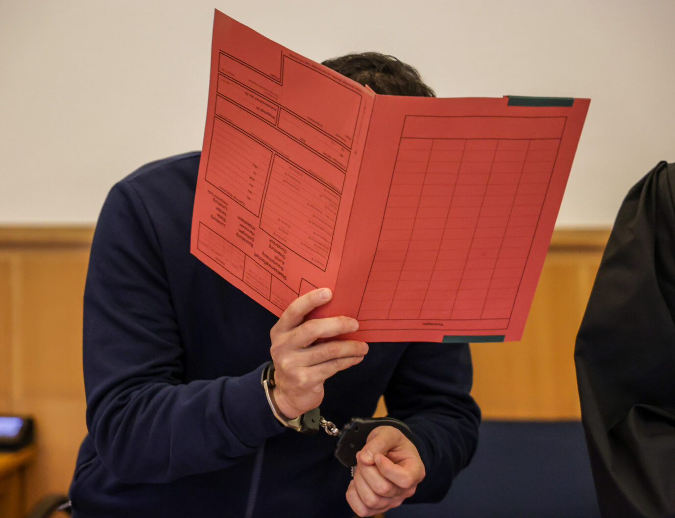 Der verurteilte Miri-Clan-Mörder versteckt sich hinter einer Aktenmappe. Das Urteil lautet lebenslange Haft.