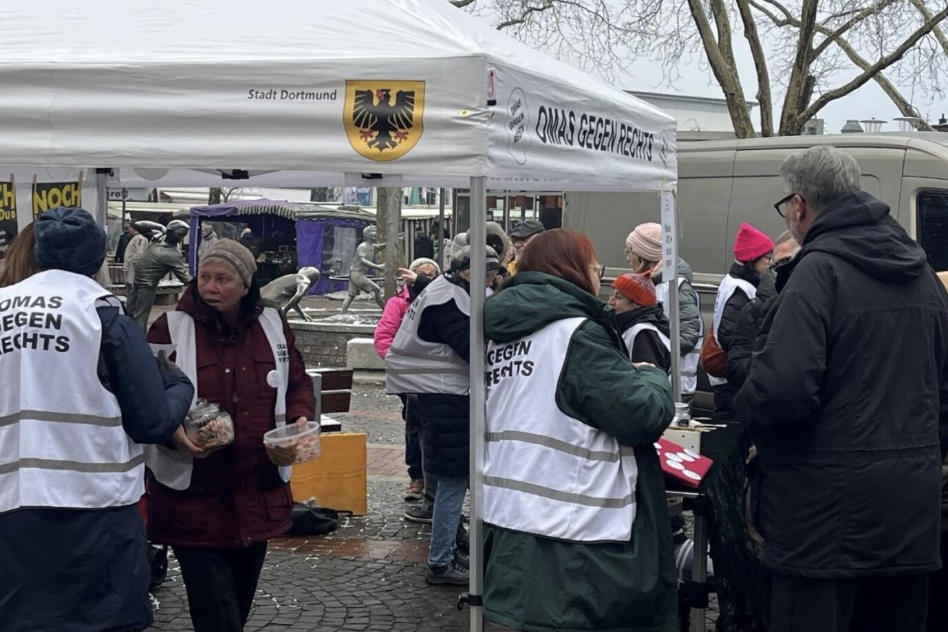 Ein weißes Zelt der Initiative „Omas gegen rechts“ mit dem Stadtwappen Dortmunds und der Aufschrift „Stadt Dortmund“ steht auf einem Platz. Mehrere Personen in weißen Westen mit dem Logo der Initiative verteilen Material und sprechen mit Passanten. Zelt mit Stadtwappen: Die „Omas gegen rechts“ durften damit gegen die AfD auftreten – bezahlt aus städtischen Mitteln.