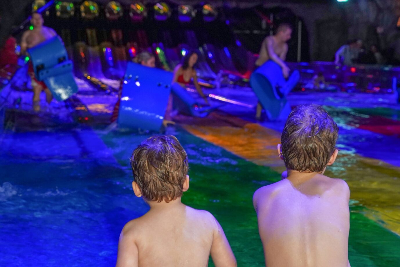 Zwei Kinder stehen in Badebekleidung am Startbereich der neuen Rennrutsche „Vikingløp“ in der Wasserwelt Rulantica in Rust, während im Hintergrund andere Besucher auf farbigen Matten in die beleuchteten Röhrenrutschen starten. Aufnahme vom 8. Februar 2023. In Rust soll ein Rumäne ein sechsjähriges Mädchen aus einem Erlebnisbad in ein Waldstück gelockt und zu sexuellen Handlungen gezwungen haben. Die Ermittler identifizierten einen 31jährigen Tatverdächtigen, der flüchtig ist. Hinweise nimmt die Polizei weiter entgegen. Kinder im Erlebnisbad Rulantica: Eine Sechsjährige wurde weggelockt und mißbraucht. Foto: IMAGO / HOFER