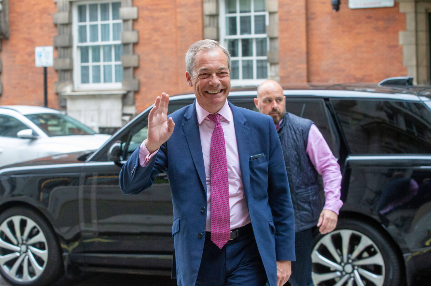 Der Vorsitzende der Reform Uk, Nigel Farage, lächelt und hebt grüßend die Hand