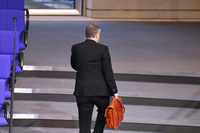Ein Mann im schwarzen Anzug geht mit einer braunen Aktentasche in der Hand eine Treppe im Bundestag hinauf, fotografiert von hinten. Robert Habeck auf dem Weg aus dem Bundestag: Der Grünen-Politiker legt sein Mandat nieder. Foto: IMAGO / dts Nachrichtenagentur