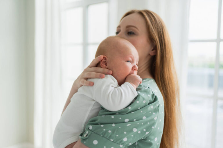 Eine rothaarige Mutter in einem türkisen Kleid hält ihr Baby im Arm – laut neuen wissenschaftlichen Erkenntnissen wird sie ihr Leben durch ihr Kind als sinnvoller erleben