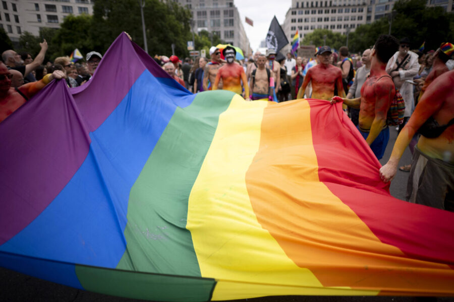Teilnehmer des Christopher Street Day in Berlin halten gemeinsam eine große Regenbogenfahne. Im Hintergrund stehen bunt bemalte Menschen, viele mit nacktem Oberkörper, einige mit Flaggen oder Transparenten. Die Szene spielt sich auf einer gesperrten Straße zwischen Hochhäusern ab. Bunt angemalte Männer tragen eine Regenbogenflagge: Auch der Bundestag war beim CSD dabei. Foto: IMAGO / IPON