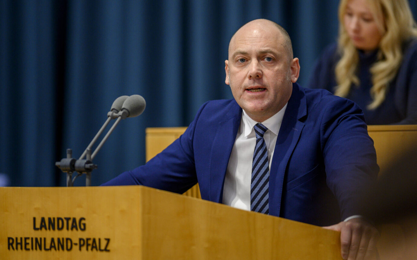 AfD-Politiker Joachim Paul spricht am Rednerpult im Landtag Rheinland-Pfalz, vor ihm zwei Mikrofone, im Hintergrund unscharf eine sitzende Frau. Joachim Paul im Landtag Rheinland-Pfalz: Der AfD-Politiker wehrt sich juristisch gegen seinen Ausschluß von der Oberbürgermeisterwahl in Ludwigshafen. Foto: IMAGO / Torsten Silz