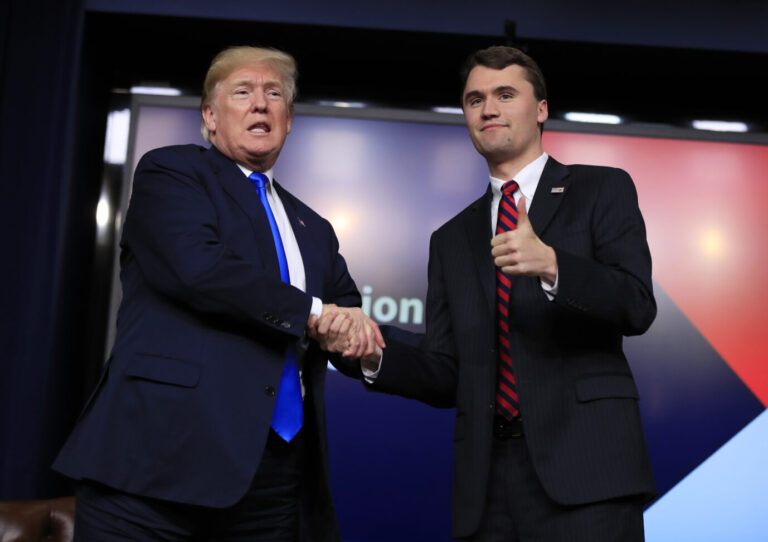 Links ist US-Präsident Donald Trump zu sehen und gibt dem rechts von ihm stehenden rechten Influencer Charlie Kirk die Hand