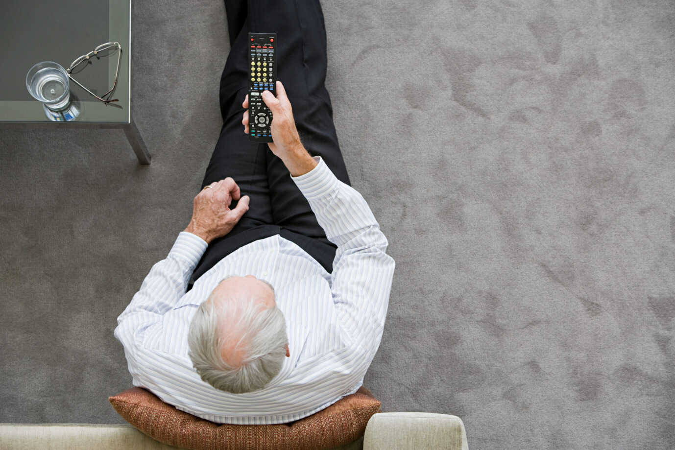 Die Kamera zeigt einen älteren Mann – von oben –, der auf einem Sofa sitzt und Fernsehen guckt. Falls er eine Sendung der öffentlich-rechtlichen schaut, wird er ihr vermutlich nicht vertrauen