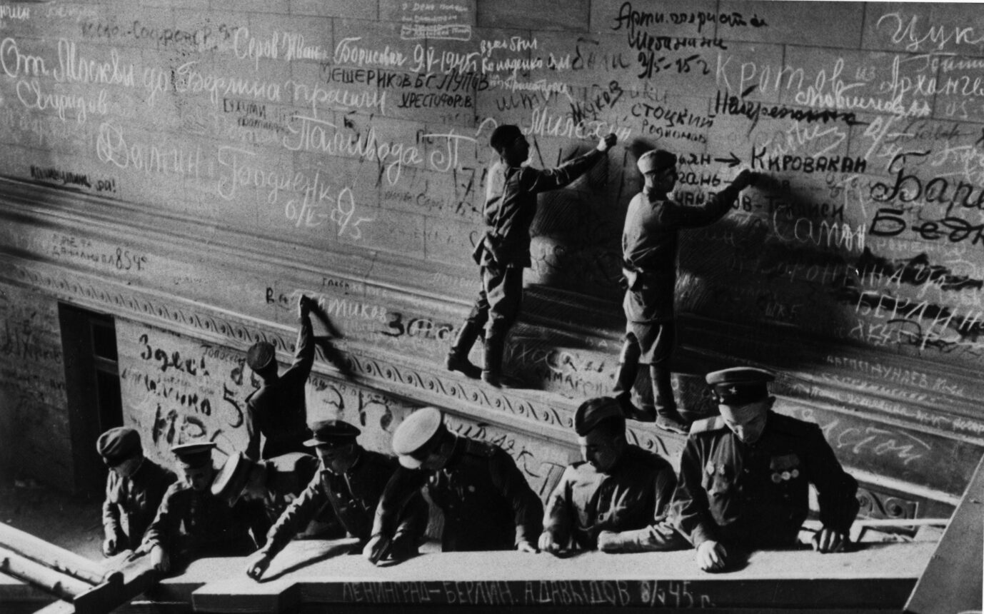 Mehrere sowjetische Soldaten in Uniform schreiben 1945 mit Kreide und Farbe ihre Namen und Botschaften auf die Innenwände des Reichstagsgebäudes in Berlin. Sowjetische Soldaten im Mai 1945: Ihre Graffiti im Reichstagsgebäude wurden in den neunziger Jahren konserviert. Foto: picture alliance / akg-images | akg-images