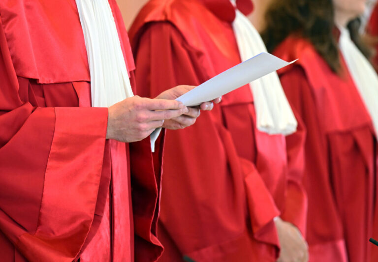Richter des Bundesverfassungsgerichts in roten Roben halten ein Schriftstück während einer Verhandlung in Karlsruhe. Der Erste Senat des Bundesverfassungsgericht verkündet das Urteil zu ärztlichen Zwangsmaßnahmen. Laut dem Urteil ist ein Krankenhausvorbehalt bei ärztlichen Zwangsmaßnahmen teilweise verfassungswidrig. Urteilsverkündung des Bundesverfassungsgericht: Tanzverbote an Karfreitag sind verfassungskonform. Foto: picture alliance/dpa | Uli Deck