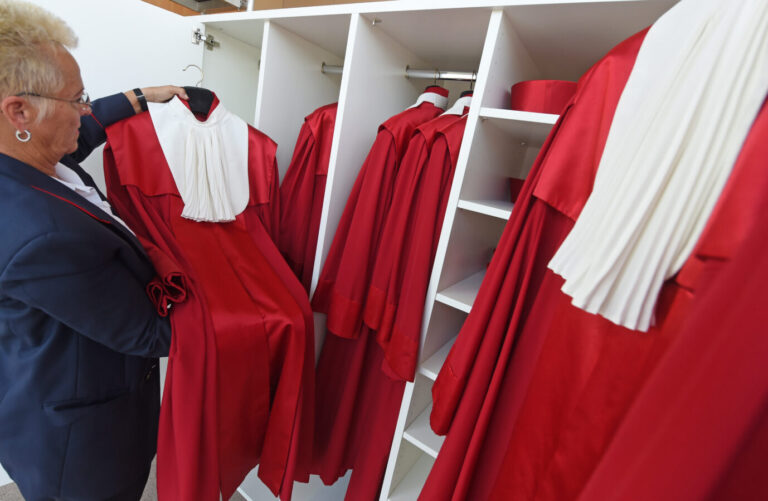 Eine Mitarbeiterin des Bundesverfassungsgerichts hängt eine rote Richterrobe mit weißem Kragen in einen Schrank, daneben sind weitere Roben ordentlich aufgereiht. – Aufgenommen 2014 beim Wiedereinzug des Gerichts in seinen sanierten Stammsitz in Karlsruhe nach dreijähriger Auslagerung. Rote Roben der Verfassungsrichter in Karlsruhe: Heute entscheidet der Bundestag über die Besetzung von drei Posten am höchsten deutschen Gericht. Foto: picture alliance / dpa | Uli Deck