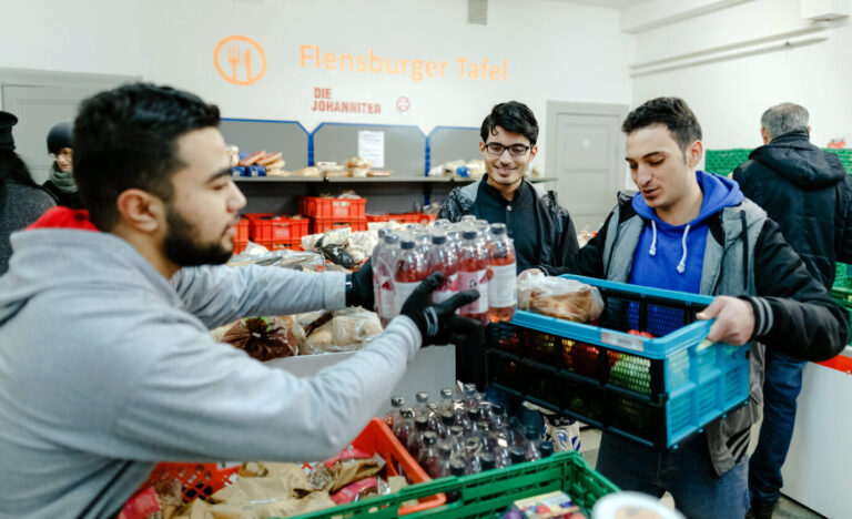 Aslan Noury (l), syrischer Praktikant, gibt am 30.12.2015 in Flensburg (Schleswig-Holstein) im Verteilraum der Flensburger Tafel, Lebensmittel unter anderem an syrische Asylbewerber aus. Aktuell wird über eine Arbeitspflicht diskutiert. Foto: Markus Scholz