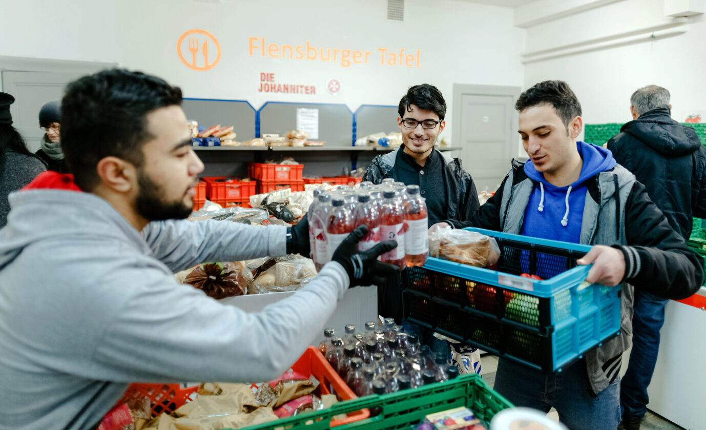 Aslan Noury (l), syrischer Praktikant, gibt am 30.12.2015 in Flensburg (Schleswig-Holstein) im Verteilraum der Flensburger Tafel, Lebensmittel unter anderem an syrische Asylbewerber aus. Aktuell wird über eine Arbeitspflicht diskutiert. Foto: Markus Scholz