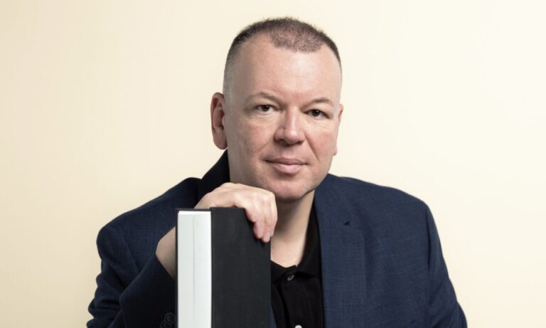 Stefan Weber, Kommunikationswissenschaftler aus Wien, sitzt an einem Tisch und lehnt sich mit der Hand an ein aufgestelltes Buch. Er trägt dunkles Sakko und schwarzes Hemd und blickt in die Kamera. Stefan Weber: Der Wiener Kommunikationswissenschaftler und Plagiatsprüfer warnt vor Kaufholds Konzept einer „Systemaufsicht“. Foto: Joachim Bergauer Er ist der Plagiatsjäger.
