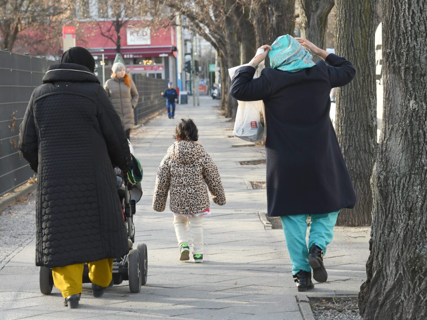 Zwei Frauen mit Kopftuch gehen mit einem Kinderwagen und einem Kind eine Straße in Berlin-Kreuzberg entlang, aufgenommen am 28. Februar 2017. Straßenszene in Berlin-Kreuzberg: Die Familienkasse zahlte 2024 mehr als 57 Milliarden Euro Kindergeld und Kinderzuschlag aus. Foto: picture alliance / Winfried Rothermel | Winfried Rothermel