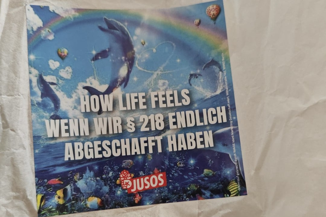 Bunter Aufkleber der SPD-Jugendorganisation Jusos mit springenden Delfinen, Regenbogen und Unterwasserlandschaft. Darauf der Slogan „How Life feels – Wenn wir Paragraph 218 endlich abgeschafft haben“. Aufkleber der Jusos mit Delfin-Motiv: Vor der Gesamtschule Rodenkirchen wurde er auch an Zehnjährige verteilt. Foto: AfD Köln