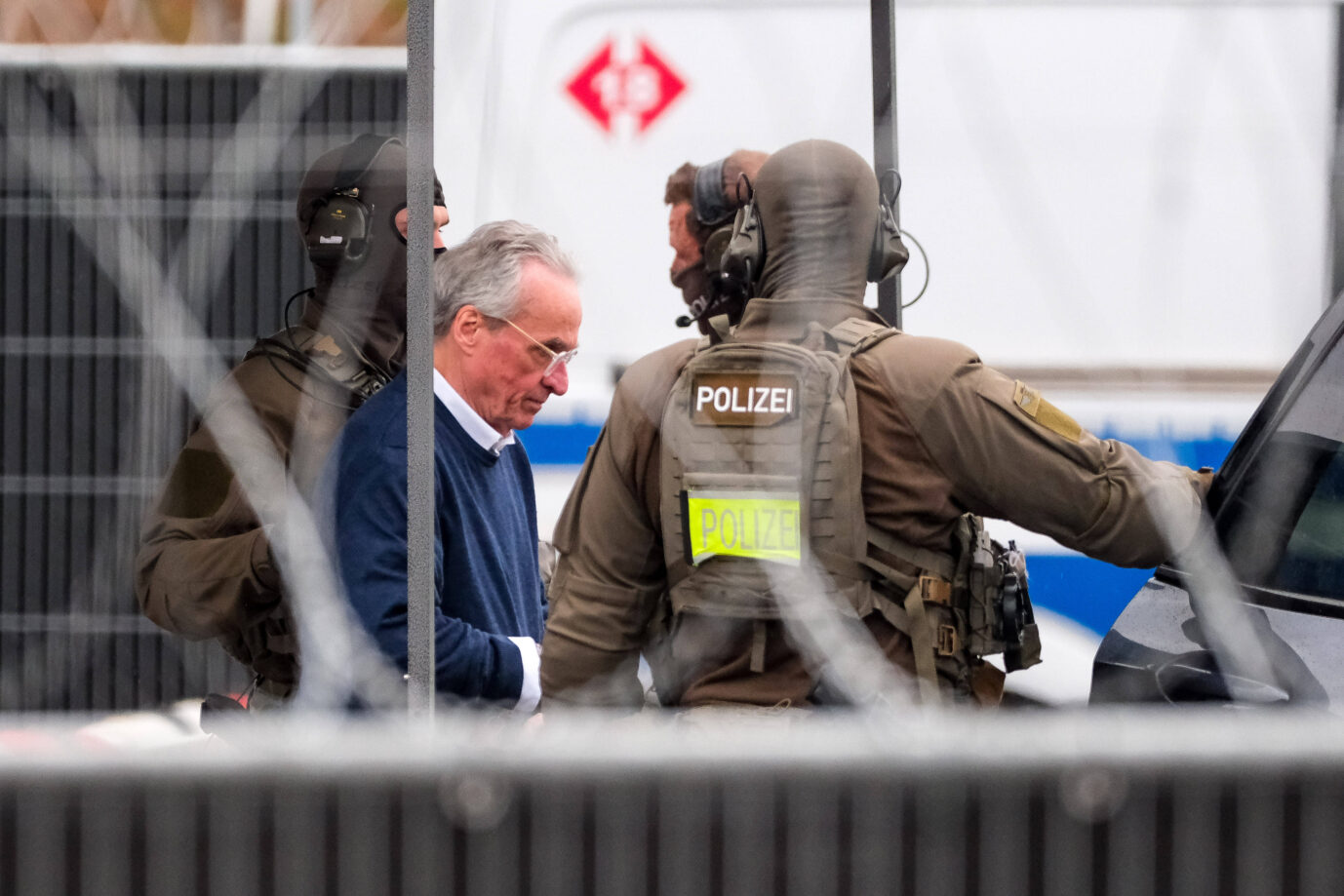 Drei uniformierte und vermummte Polizisten umringen Heinrich XIII. Prinz Reuß und bringen ihn zur Verhandlung.