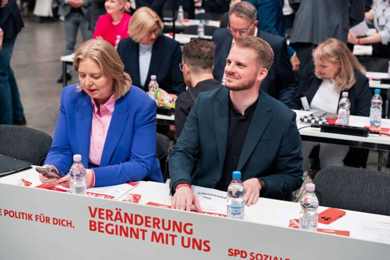 Tim Klüssendorf und Bärbel Bas sitzen nebeneinander am Tisch auf dem SPD-Bundesparteitag 2025. Vor ihnen ein Schild mit dem Motto ‚Veränderung beginnt mit uns‘. SPD-General Tim Klüssendorf neben Sozialstaatsministerin Bärbel Bas auf dem Bundesparteitag: „Veränderung beginnt mit uns“. Foto: IMAGO / Stefan Zeitz