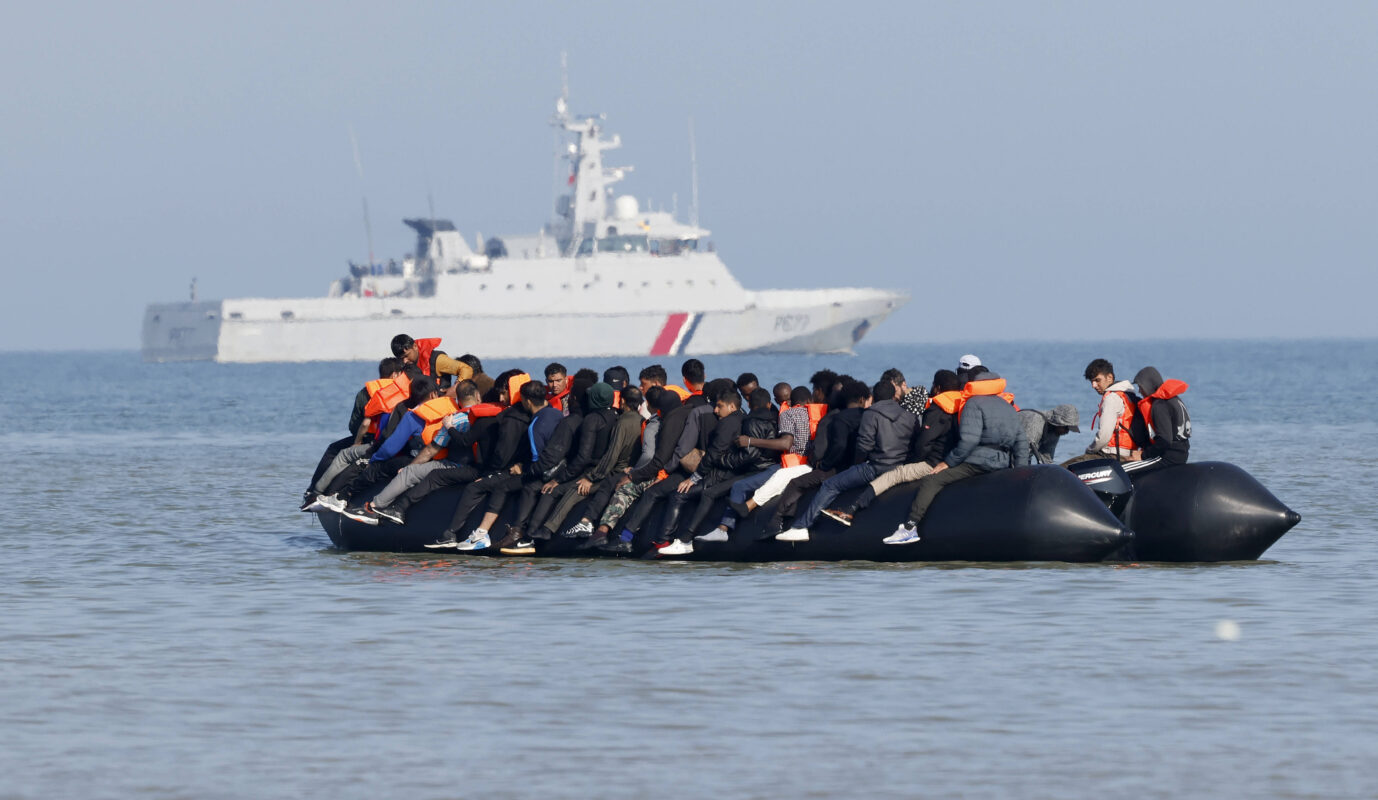 Auf einem Schluachboot auf dem Wasser sitzen Dutzende dunkelhäutige Asylbewerber und wollen über den Ärmelkanal nach Großbritannien – Nigel Farage verspricht dagegen vorzugehen