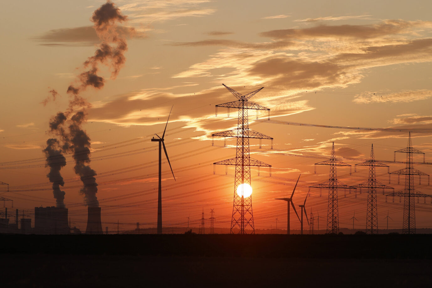 In der roten Abendsonne sieht man Windräder. Strommasten und ein Kohlekraftwerk des Stromkonzerns RWE.